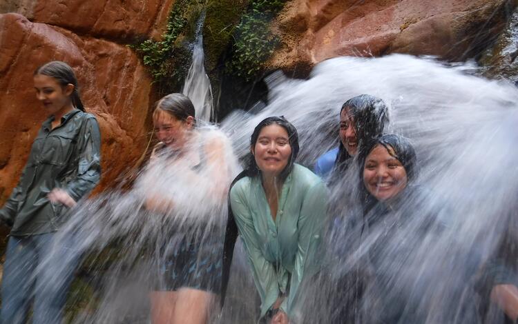 Partners in Science trip participants cool down under a small waterfall on a hot day