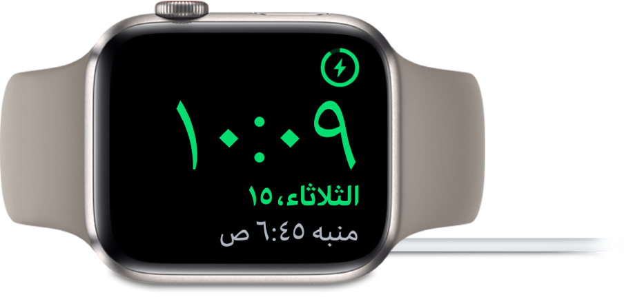 Apple Watch موضوعة على جانبها ومتصلة بالشاحن، وتعرض الشاشة رمز الشحن في الزاوية العلوية اليمنى، والوقت الحالي أسفل ذلك، ووقت المنبه التالي.