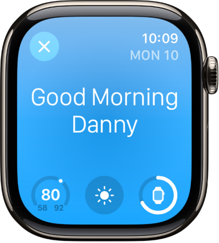 Apple Watch menampilkan layar bangun. Kata Selamat Pagi muncul di bagian atas. Suhu, kondisi cuaca, dan level baterai ada di bawah.