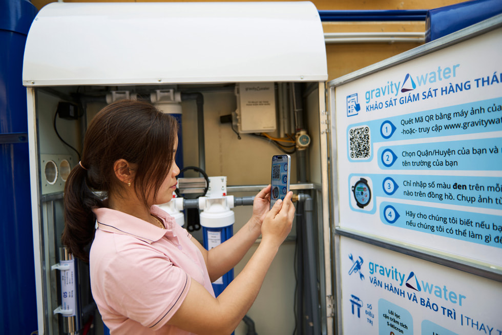 Eine Schülerin hält ein iPhone hoch, um einen QR-Code auf einem Gravity Water-Schild an der Vay Nua Primary and Secondary Boarding School for Ethnic Minorities zu scannen.
