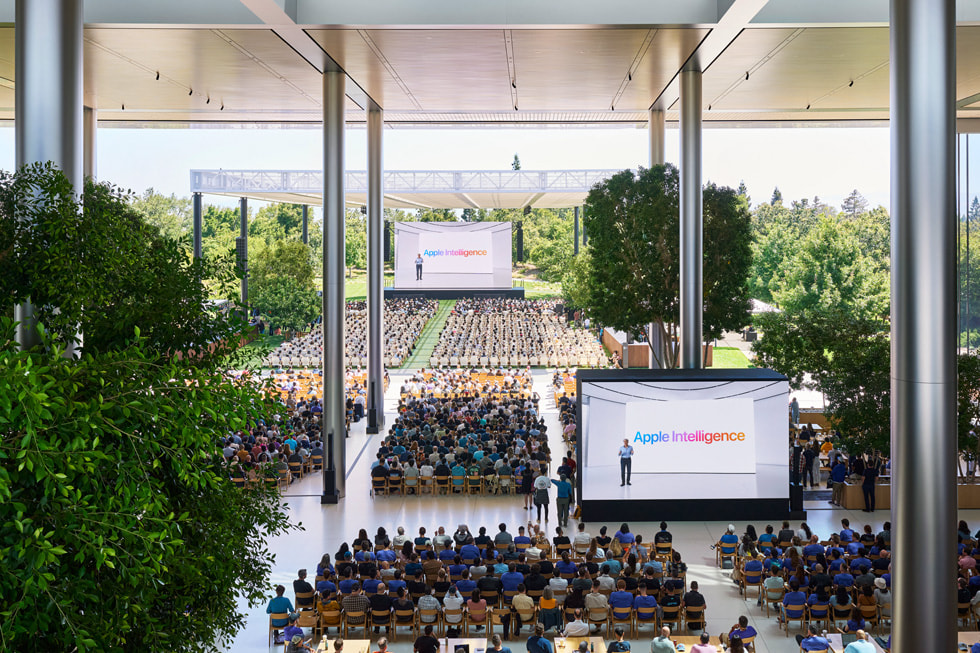 Luftaufnahme der Entwickler:innen, die die Keynote auf großen Leinwänden im Caffè Macs im Apple Park anschauen. 