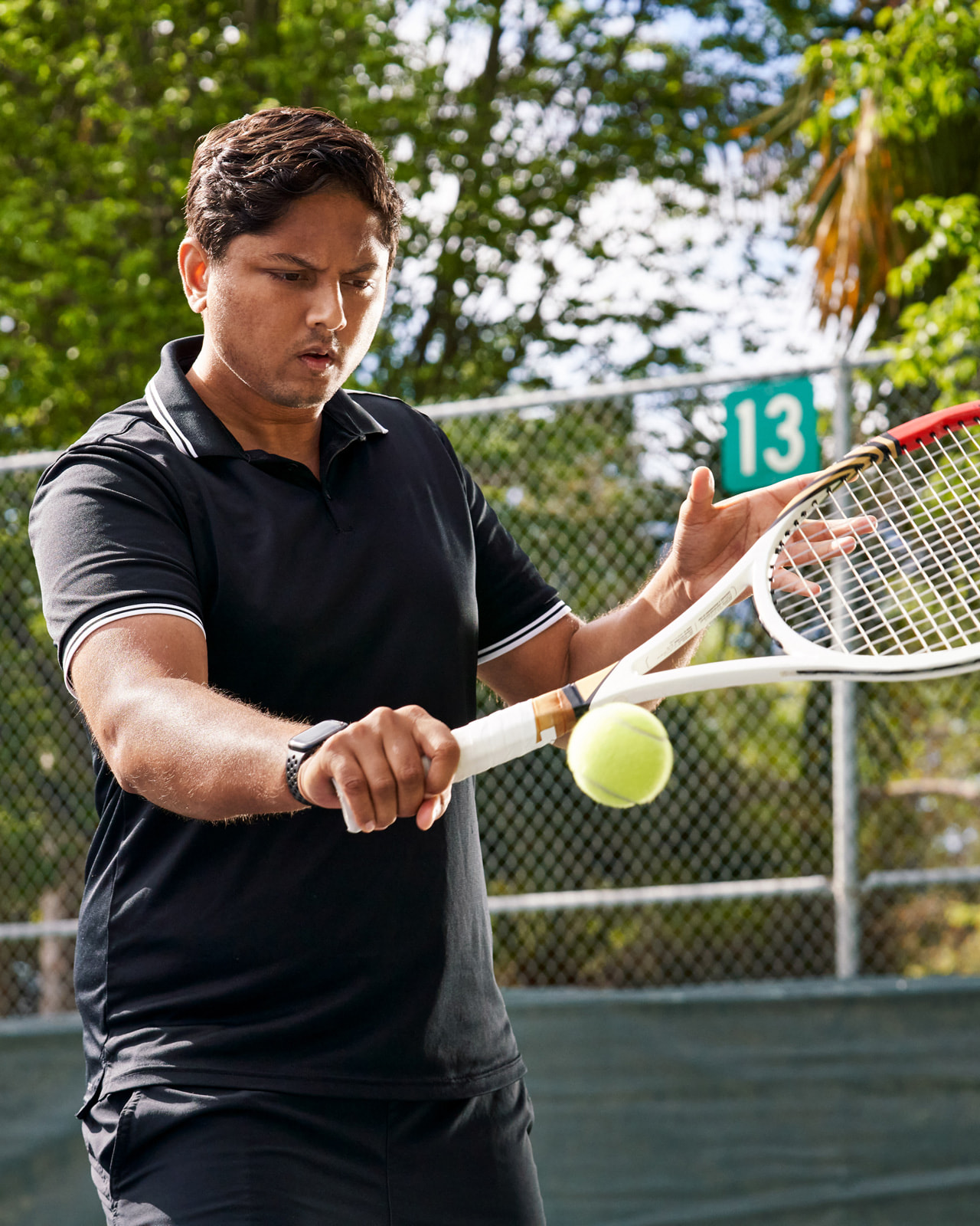 Sahai staat op de tennisbaan en speelt een tennisbal met de backhand.