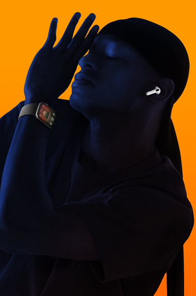 A person listening to music on an Apple Watch wearing AirPods, with their eyes closed and leaning back with their hand raised towards their face.