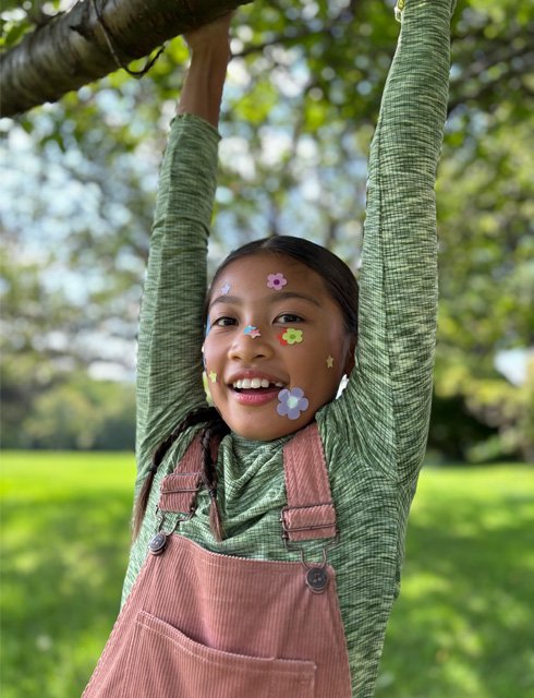 Photo en gros plan d’une jeune fille avec des autocollants de fleurs sur le visage, prise avec le Téléobjectif 2x de qualité optique de l’iPhone 15