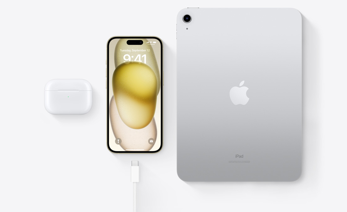 Μια πανοραμική άποψη των AirPods Pro, του iPhone 15 και ενός iPad με υποδοχή USB-C που δείχνει ότι και οι τρεις συσκευές μπορούν να φορτιστούν με το ίδιο καλώδιο USB-C.