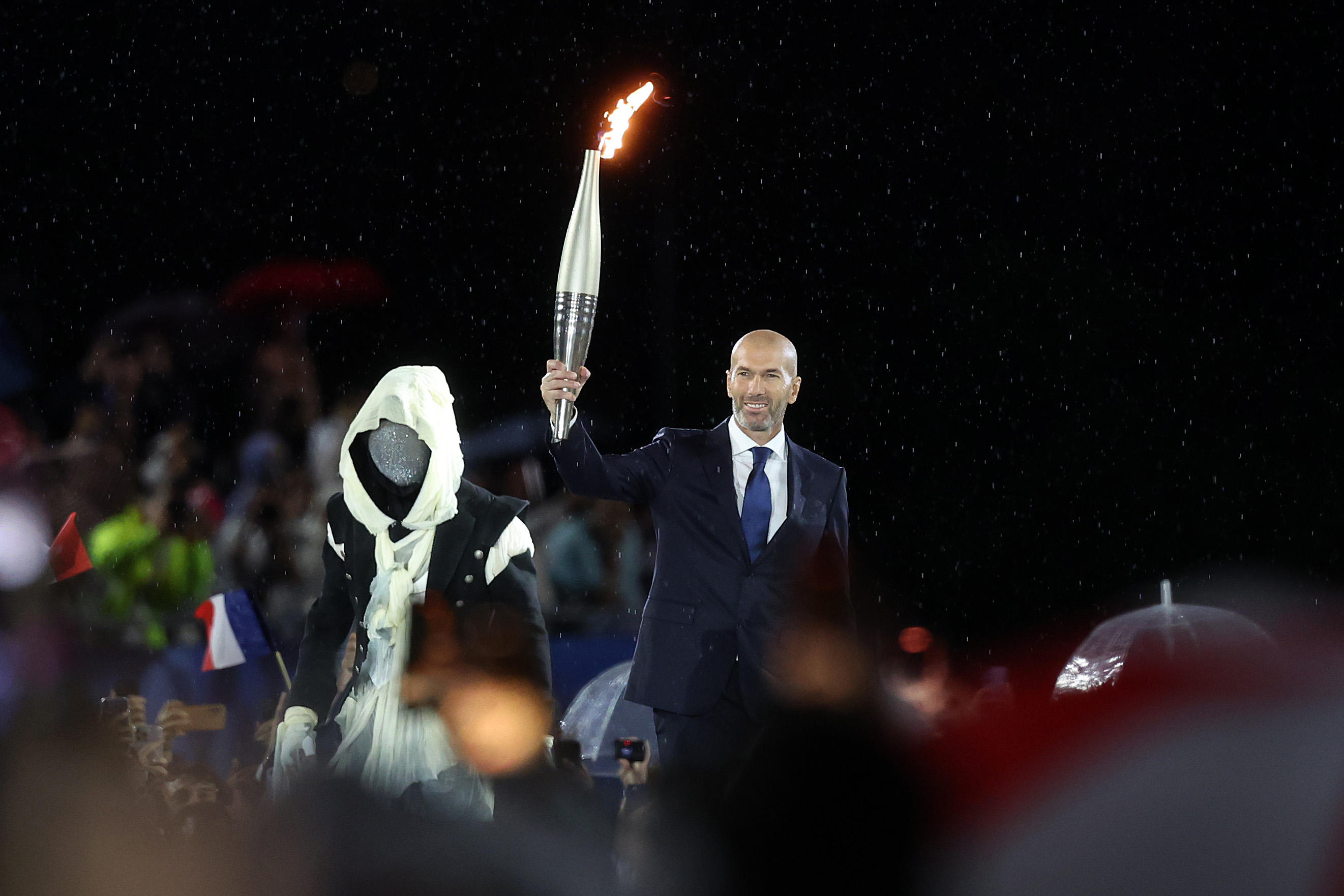 L'homme masqué a apporté la flamme olympique à Zinedine Zidane. Icon Sport