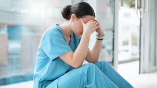 Stock image of a nurse sitting with her hands over her face.