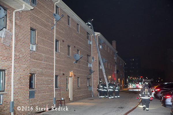 firefighters with ground ladder to roof of apartment building