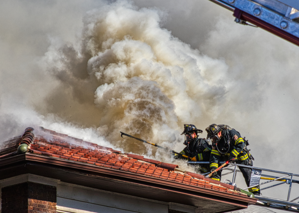 dramatic photo of Cicero Firefighters venting a roof in heavy smoke from aerial ladder