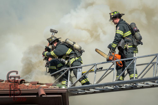 Firefighters venting a roof in heavy smoke from aerial ladder