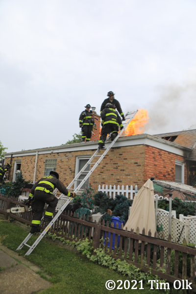 Firefighters climb ladder to roof with flames