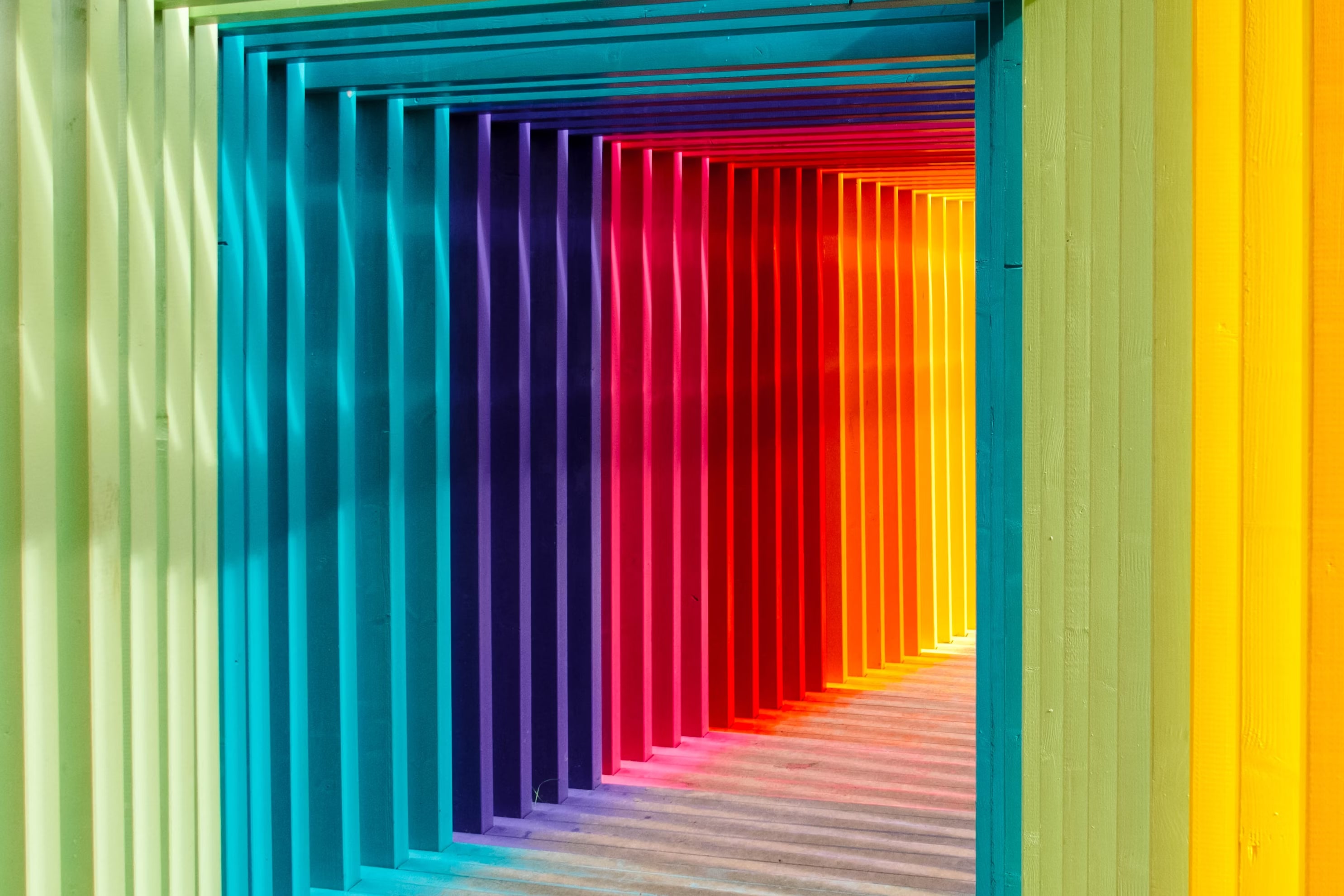 A corridor of multi-colors frames, creating a rainbow hallway, is well lit and the light is blending colors inside the corridor.