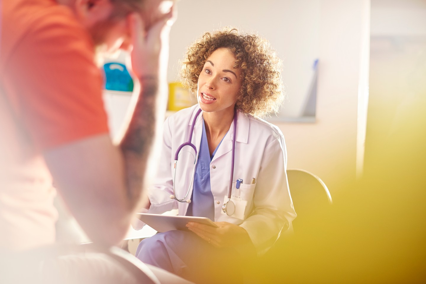 Doctor in white coat speaking with tattooed man in foreground