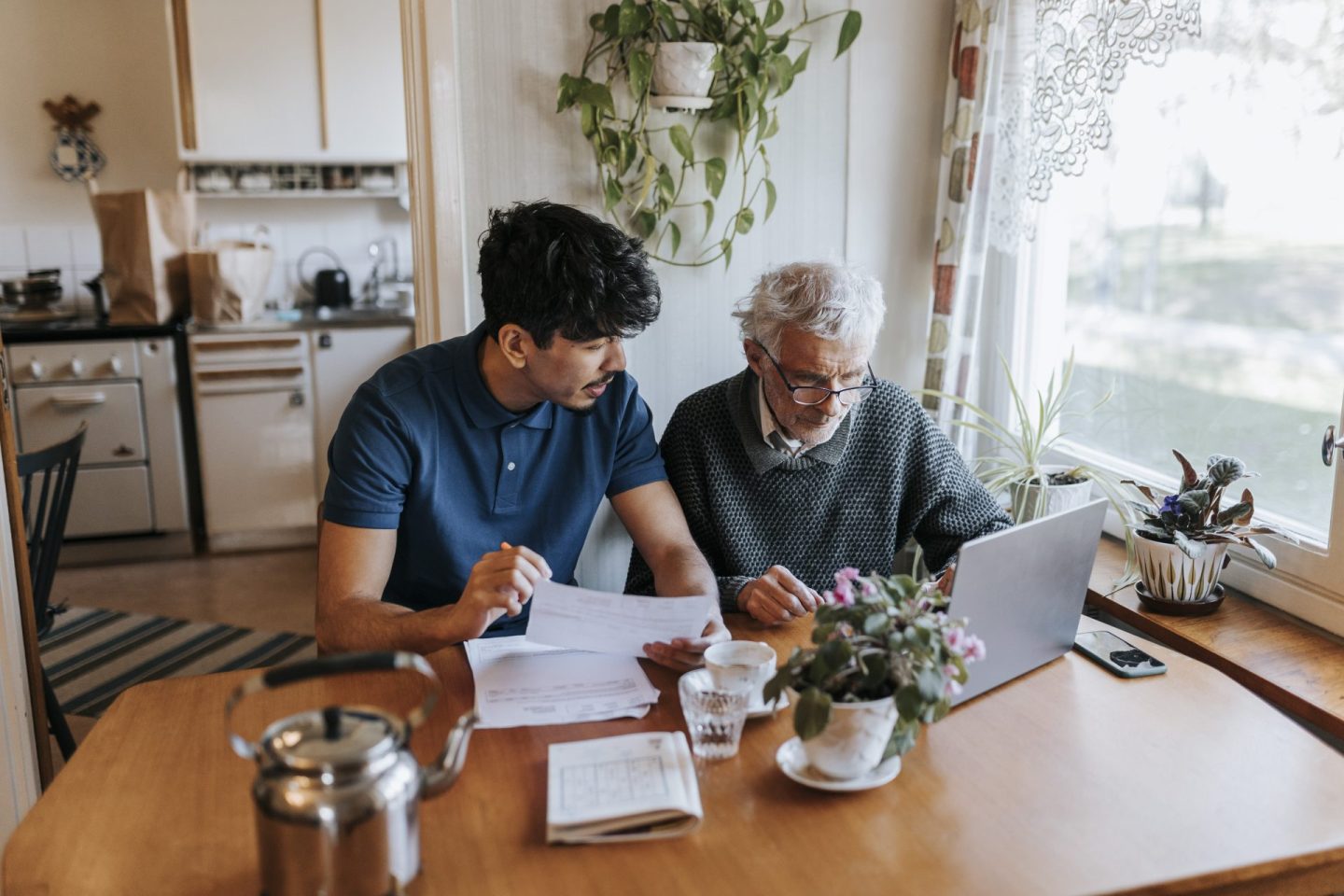 Male caregiver discussing medical reports with senior man using laptop at home