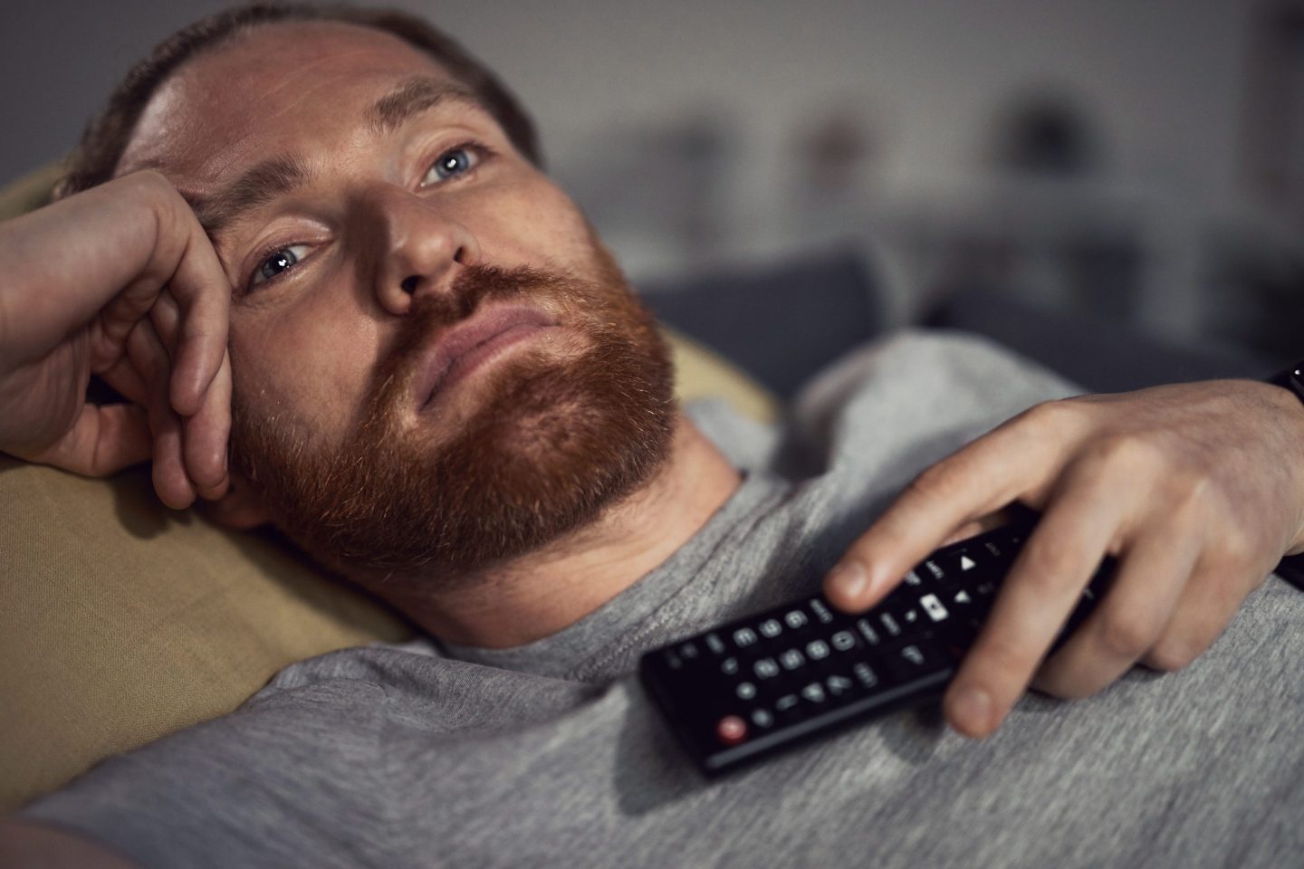 Closeup of bearded man frowning while holding TV remote on his chest