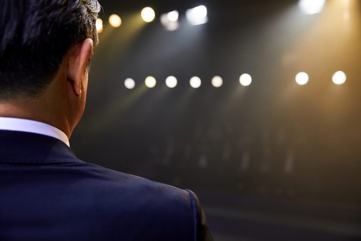 Closeup of man in suit from behind with stage lights pointing at him