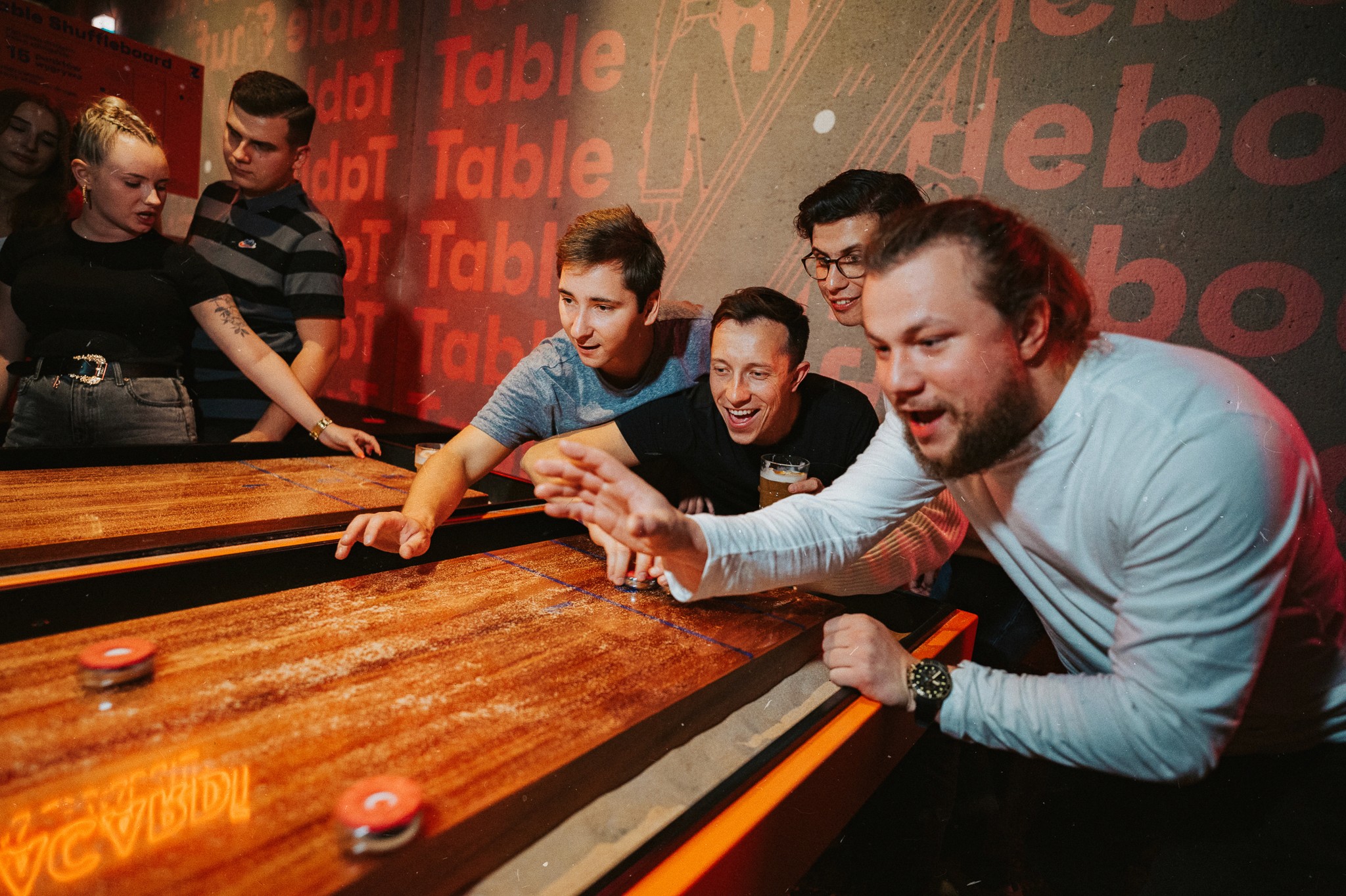 Grupa ludzi bawiących się w table shuffleboard. System rezerwacji Going. Places umożliwia łatwe zarządzanie obecnością klientów w przestrzeni aktywności poprzez funkcję overbooking