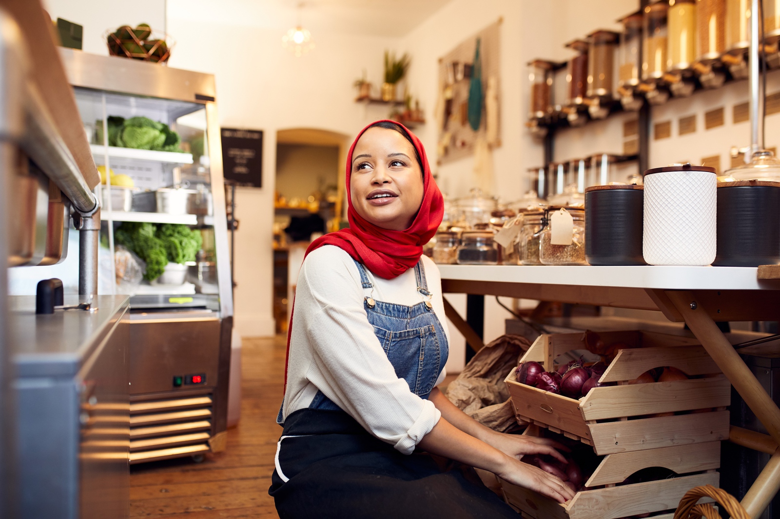 En smilende kunde i en butik fuld af tæpper, planter og keramik spørger en salgsassistent i overalls om et produkt, han sælger