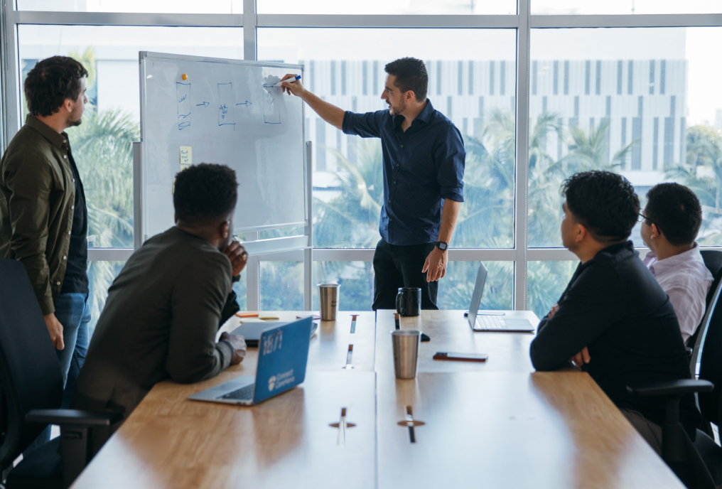 A man explaining something over white board to 4 other men