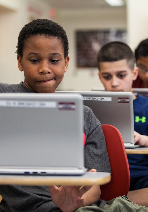 Two young boys in a classroom working on their laptops