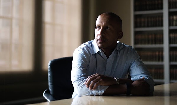 Equal Justice Initiative のエグゼクティブ・ディレクター、Bryan Stevenson。スキンヘッドの黒人男性がドレスシャツを着てデスクに座っている。