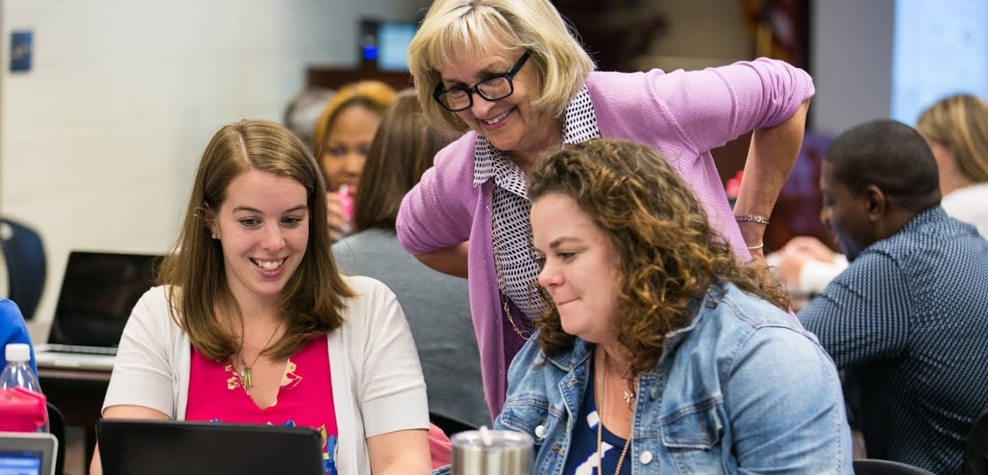 Drie vrouwen die tijdens een conferentie naar een laptopscherm kijken.