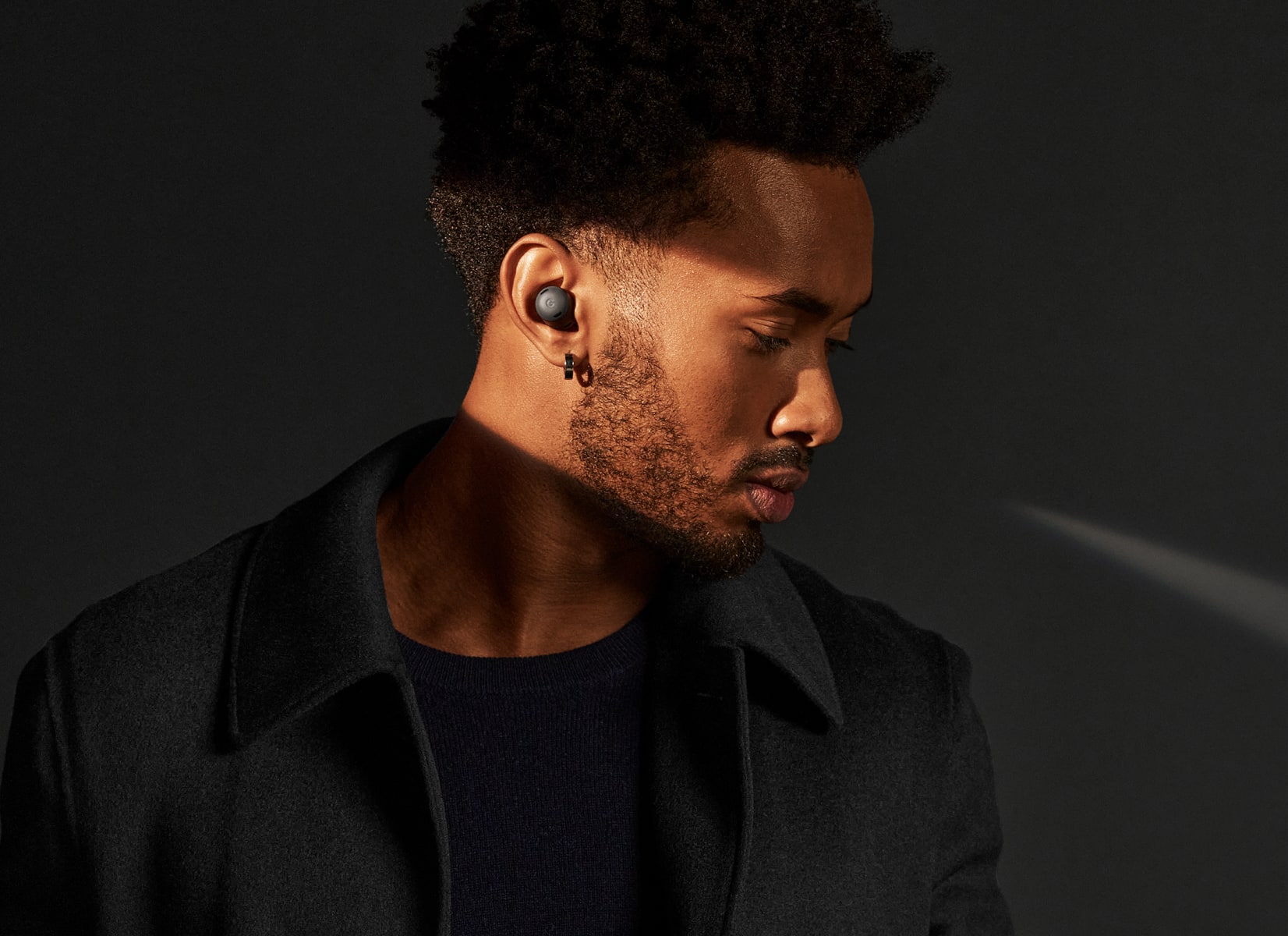 A person looks down while a ray of light illuminates the pair of Charcoal Pixel Buds Pro in their ears