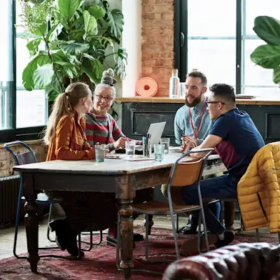 Fire kollegaer sitter ved et møtebord på et flott kontor med flere planter.