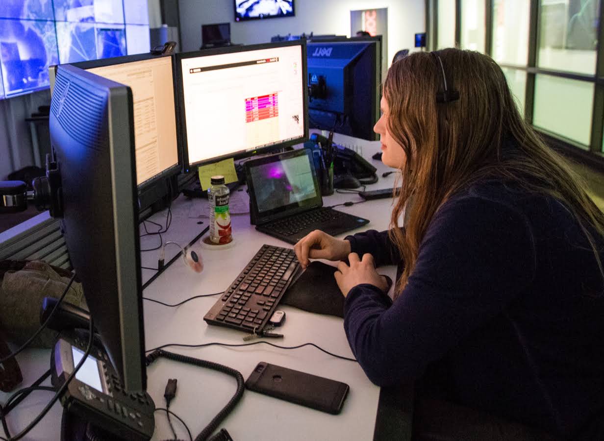 Junge Frau an einem Schreibtisch, auf dem drei Monitore stehen