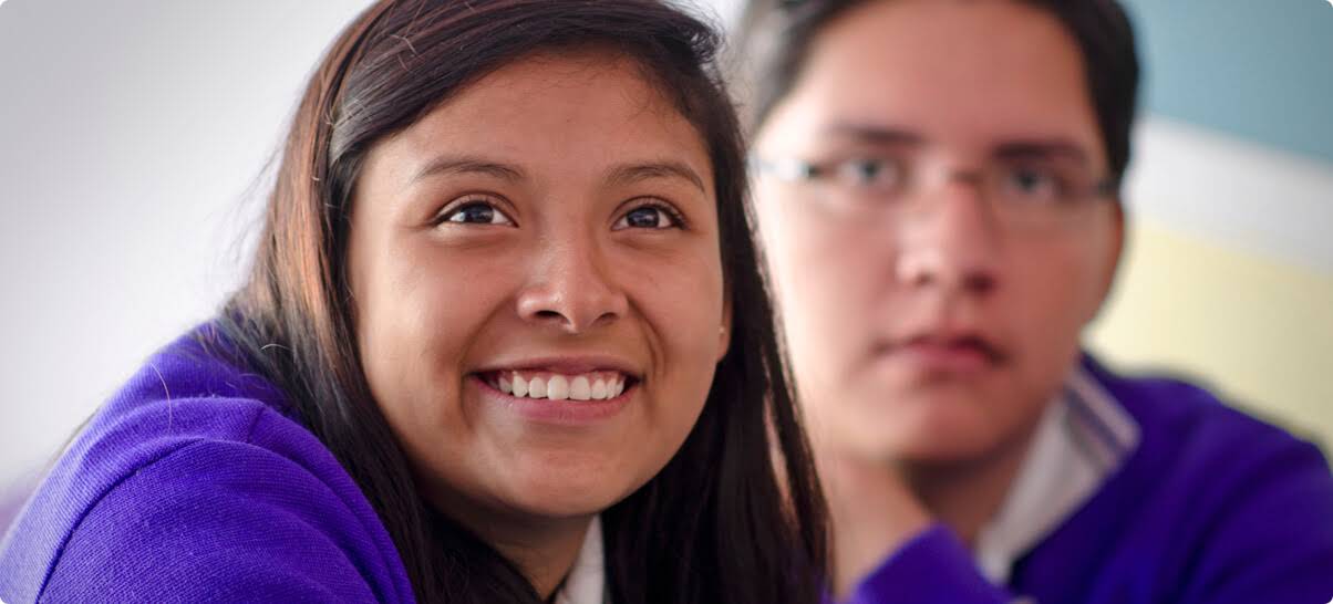 Una adolescente que mira a lo lejos, sonriente, y un adolescente serio que presta atención en el fondo