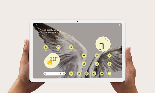 両手で持っている Google Pixel Tablet のフロント ディスプレイに天気と時刻が表示されている。