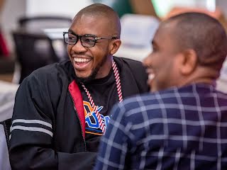 2 men laughing, 1 in focus wearing spectacles.