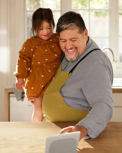 キッチンで幼い娘を抱っこした父親が、Google Nest Hub ディスプレイでレシピをチェックしています。