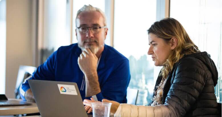 Två personer sitter vid ett bord och använder en laptop.