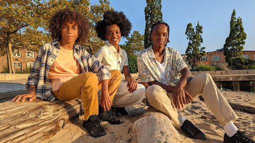 Un adolescente, un hombre y una mujer afrodescendientes sentados en un parque. El sol brilla en sus rostros.