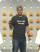 Hombre en un escenario con una camiseta en la que se lee "Hire with Google"