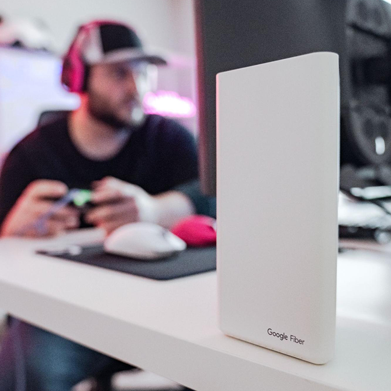 Close-up of a Google Fiber Mesh Extender with online gamer and streamer Jordan Payton in the background.
