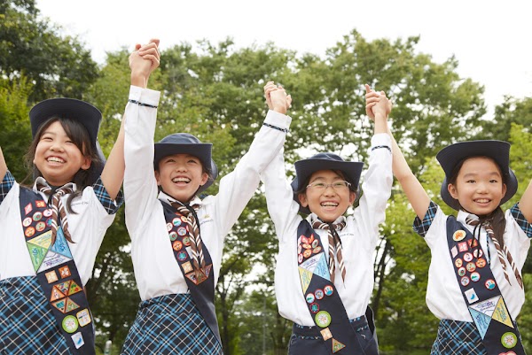4 人の日本人のガールスカウトが両手を挙げて並んで立ち、お祝いしている。