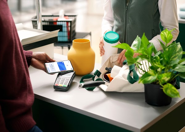 Pessoa realizando uma compra com o telefone celular. O funcionário coloca os produtos em uma sacola.