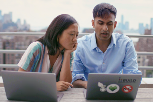 A man and woman sit at a table and work on laptops together