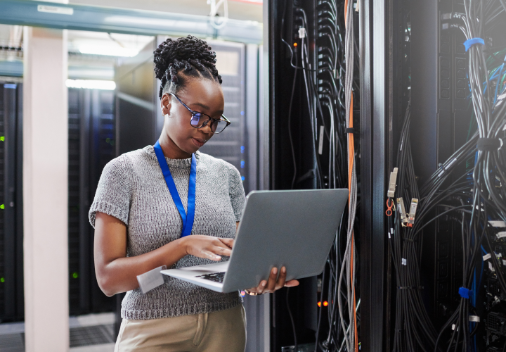 Uma mulher em uma sala de servidores olhando para o próprio computador.