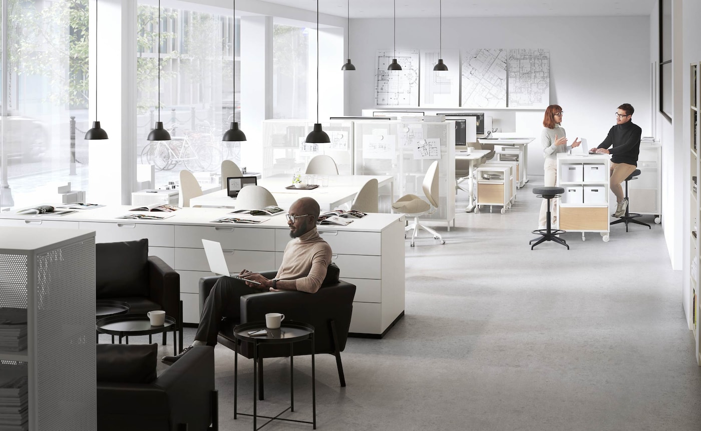 Three people are busy working in a light-filled, white office setting with grey and black accents.