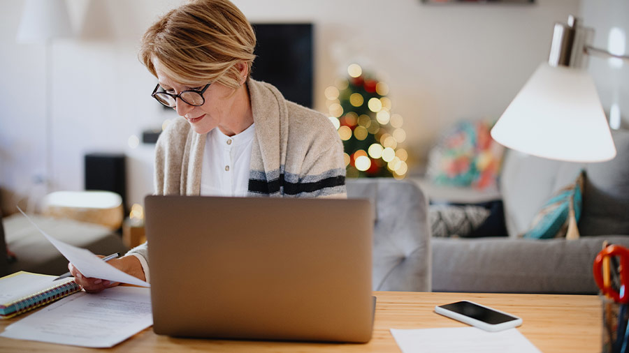 A woman sits at a desk in front of a laptop with a small business tax form.