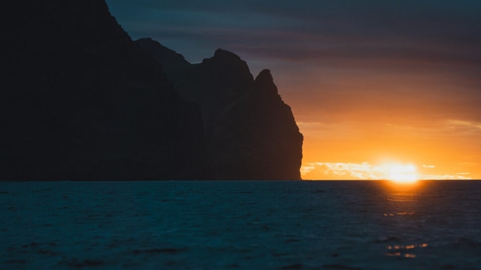 Ocean view with rock cliff and sun at the horizon.