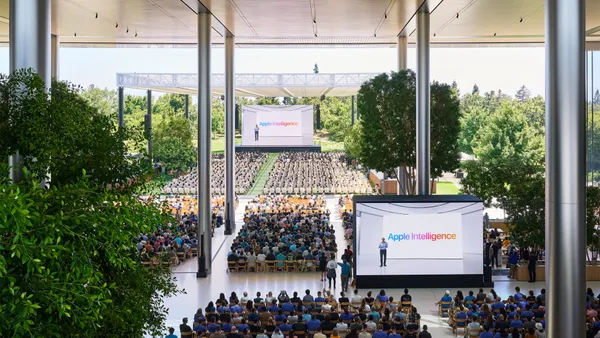 Apple WWDC 2024 attendees sit in chairs in front of a dias and two screens showing the words "Apple Intelligence."