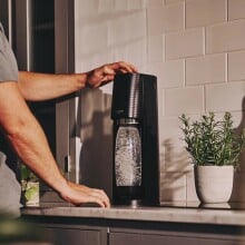 a person presses a button on the sodastream machine that sits on a counter