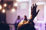 Blurred image from what seems to be a meeting or class room, where one person raises the hand to ask a question