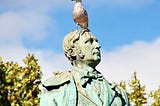 A statue of a prominent man,  with a live seagul on his head.