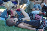 Two punks in love, on the grass in a crowd. Seemingly in a park