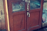 An old brown wooden cupboard, partially damaged sits comfortably at the backyard.